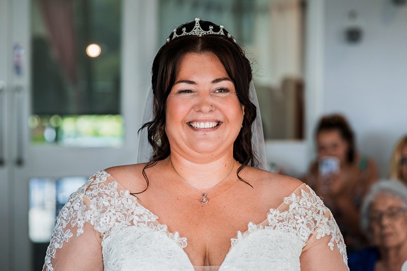 Smiling bride wearing a lacy white gown with tiara.