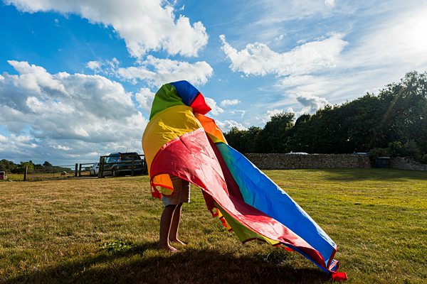 Child playing with colourful parachute outdoors.