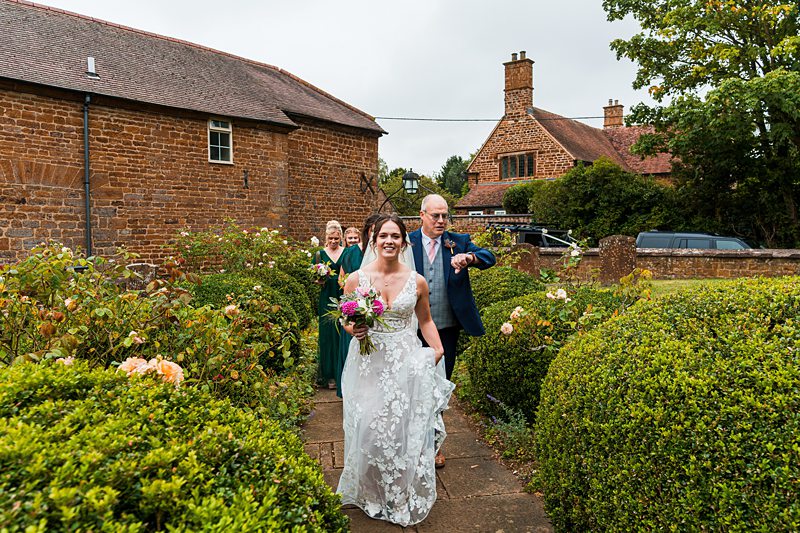 Bride walking through garden with bouquet, smiling.