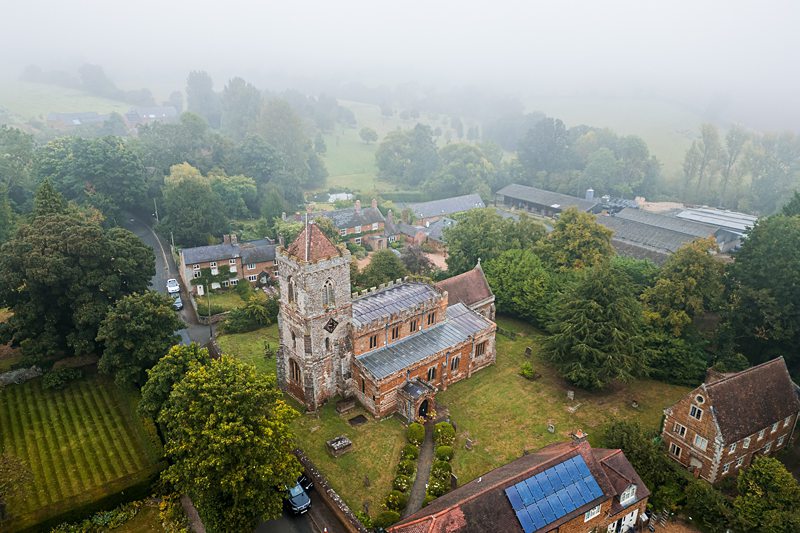 Aerial view of historic stone church in misty countryside.