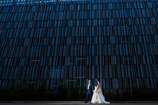 Bride and groom walk by modern building wall