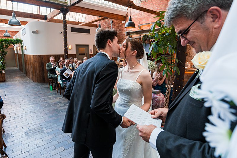 Couple kissing at indoor wedding ceremony.