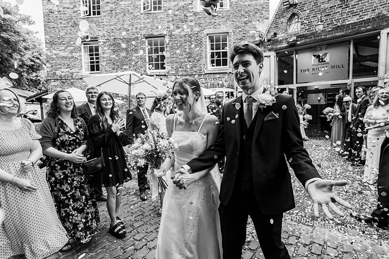 Happy wedding couple leaving ceremony with guests cheering.