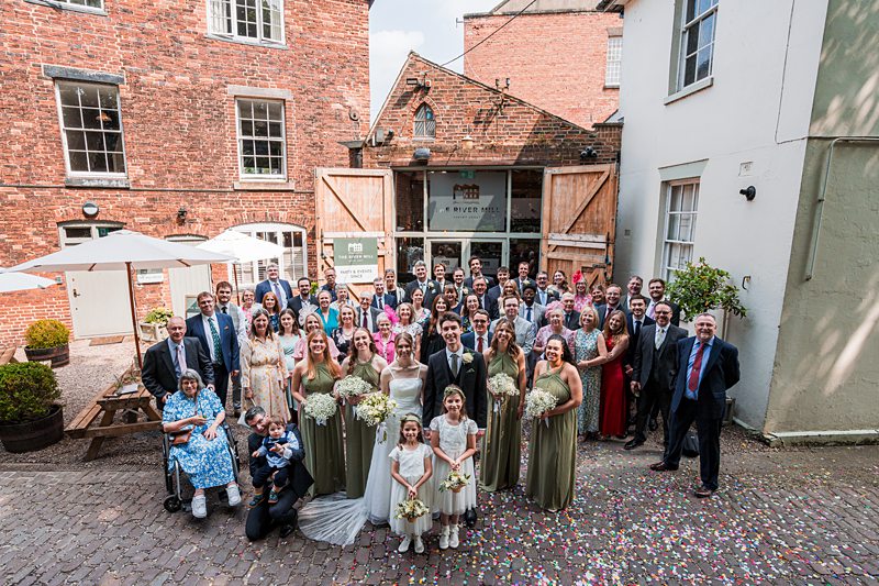 Large wedding group photo outside brick building.