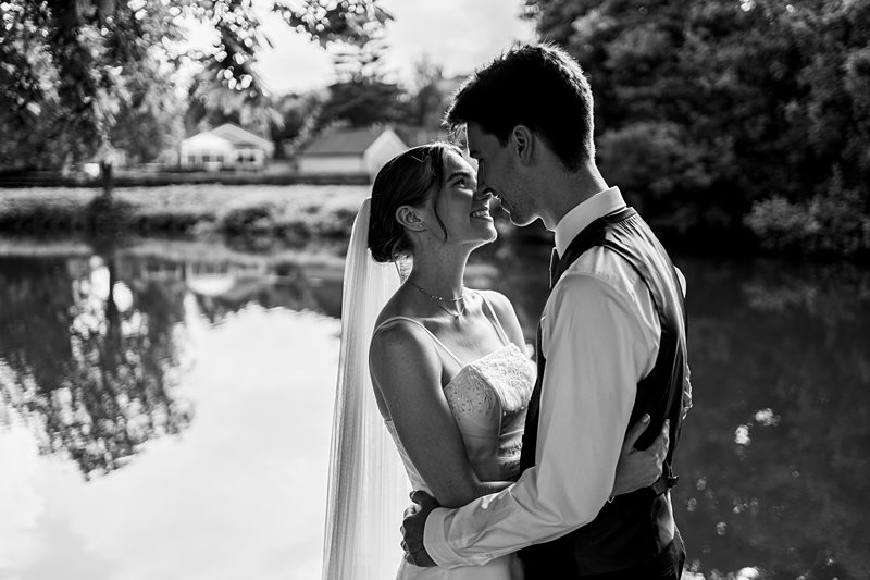 Bride and groom embracing by a lake.