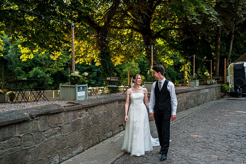 Bride and groom walking, holding hands outdoors.