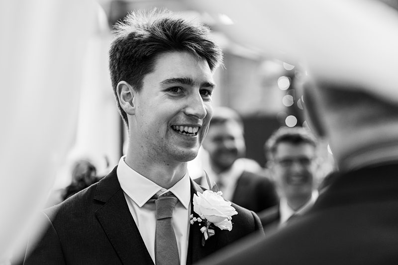 Smiling groom at wedding ceremony in black and white.