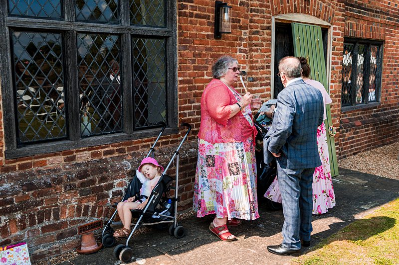 People chatting by brick building with child in pram.