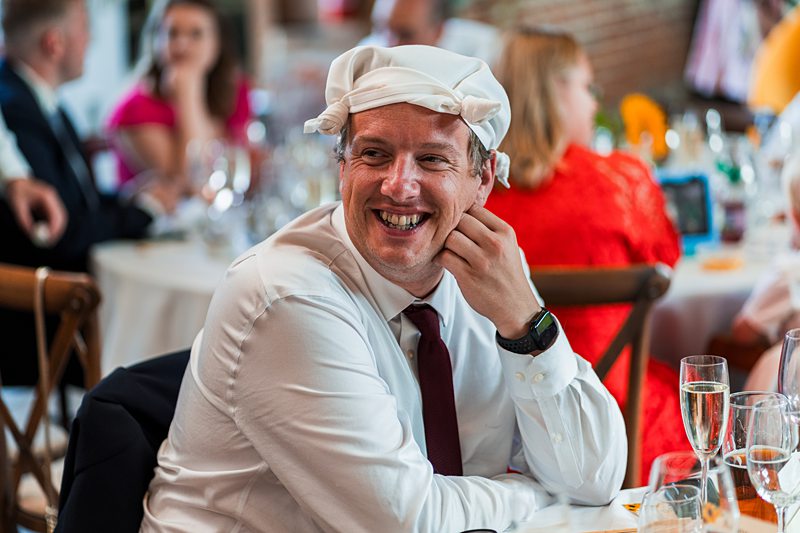 Smiling man at party wearing hat, seated at table.