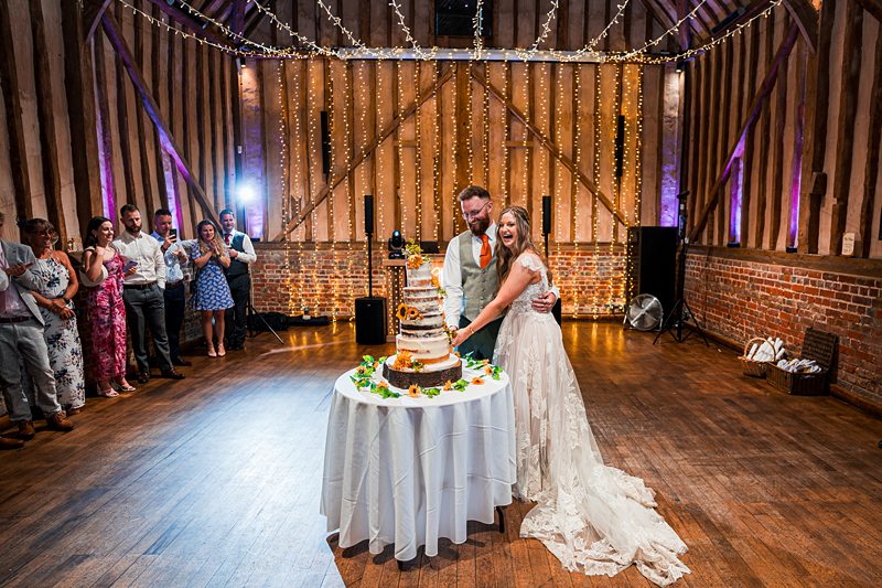 Bride and groom cut wedding cake in barn.