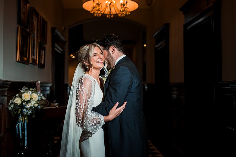 Bride and groom smiling in elegant hallway.
