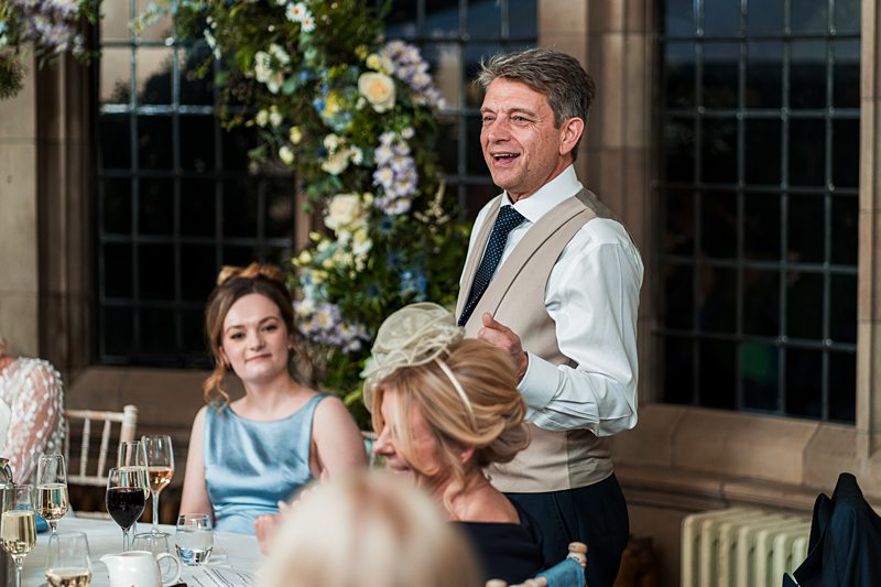 Man giving wedding speech at reception table.