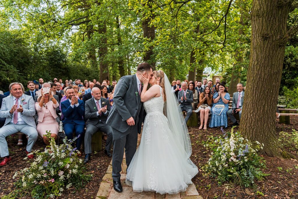 Bride and groom kissing at outdoor wedding ceremony.