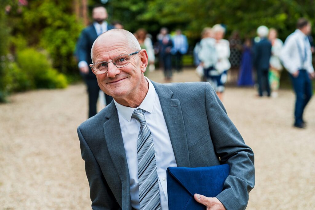 Smiling man in suit holding blue folder outside.
