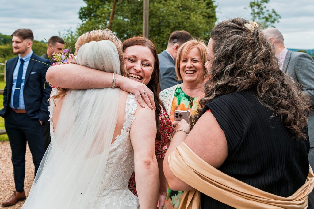 Bride hugging guests at outdoor wedding celebration.