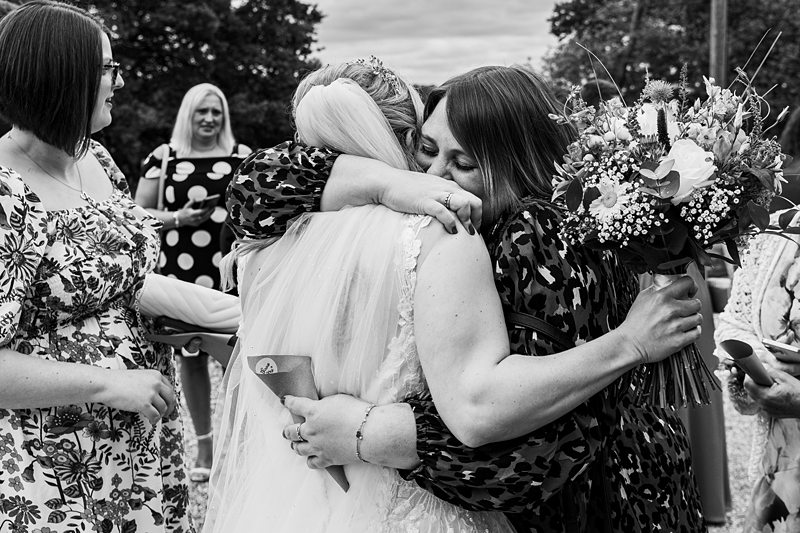 Bride hugging guest with bouquet at wedding.