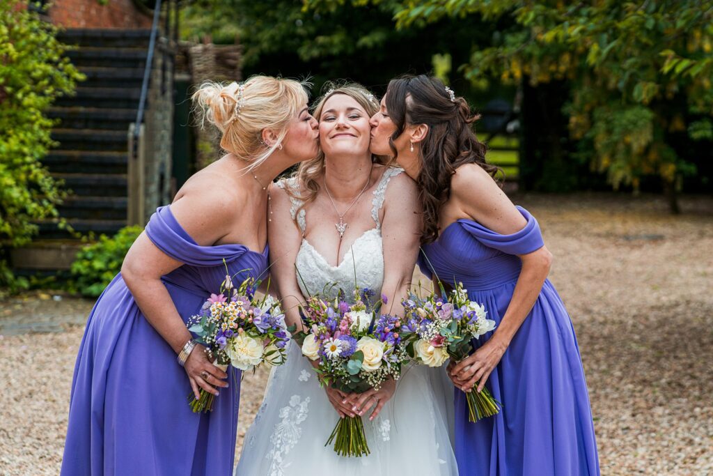 Bride kissed by bridesmaids holding bouquets