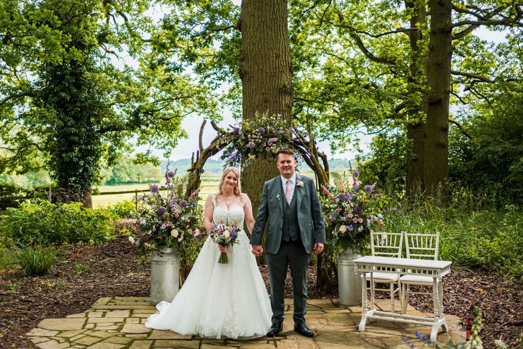 Bride and groom outdoors by floral archway.