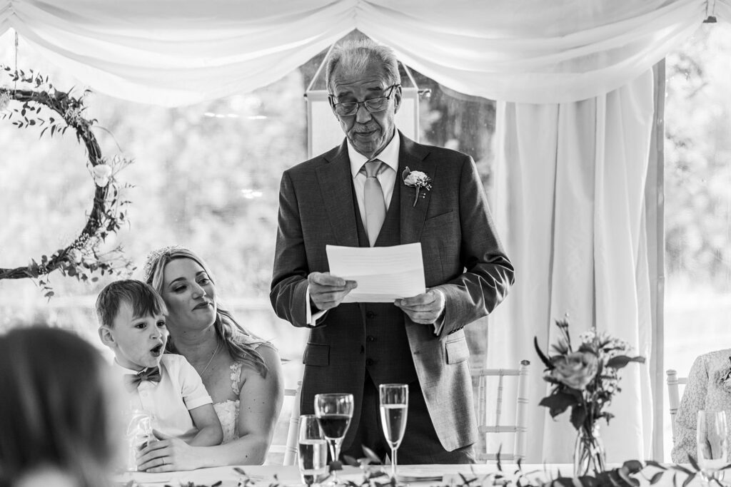 Man giving wedding speech, woman and child watching.