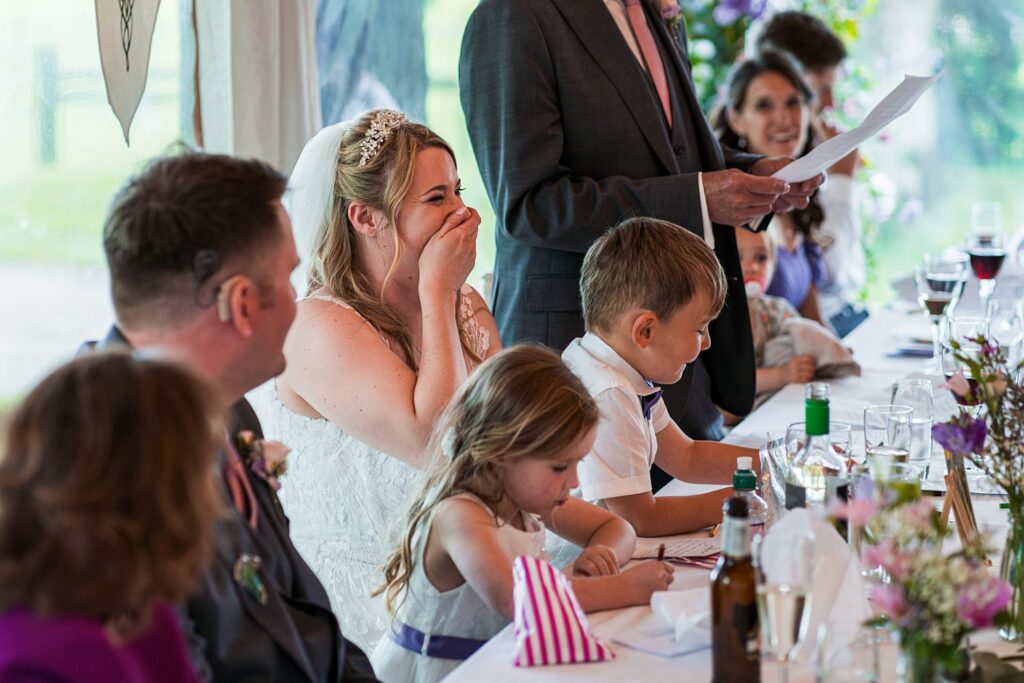 Bride laughs during wedding speech at reception.