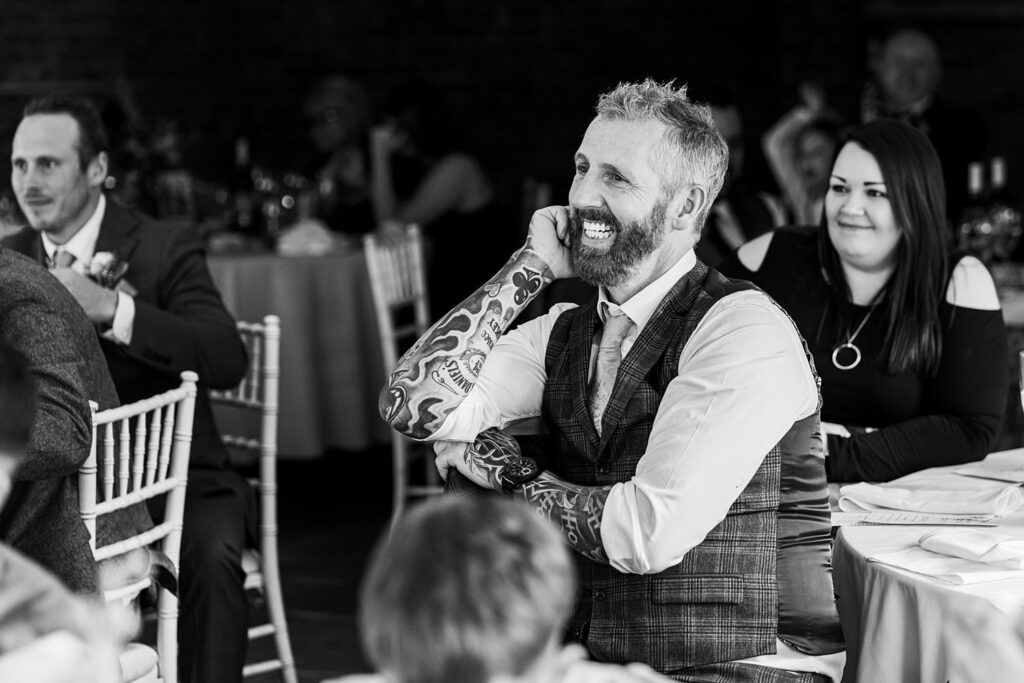 Smiling man with tattoos at a wedding reception.