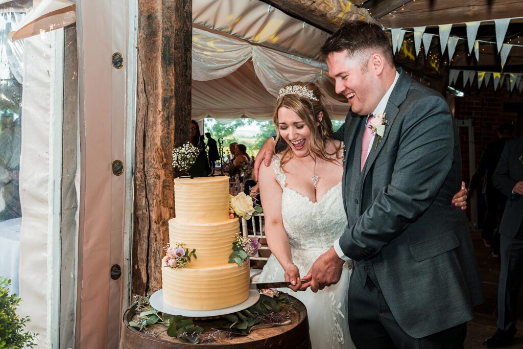 Couple cutting wedding cake together, smiling joyfully.