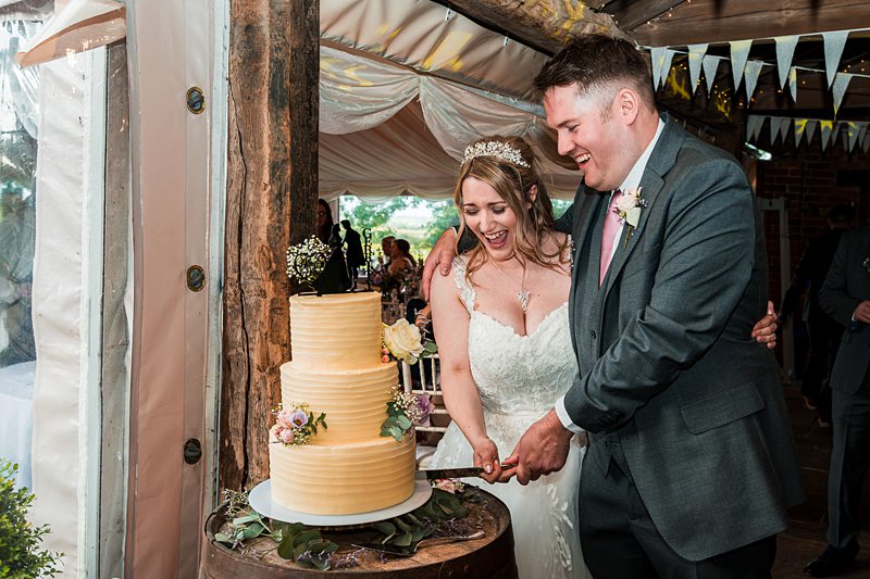 Couple cutting wedding cake together joyfully.