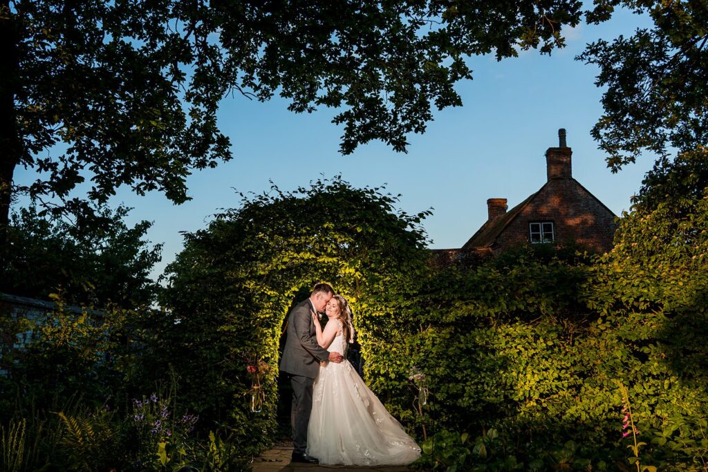 Bride and groom embrace in garden archway.