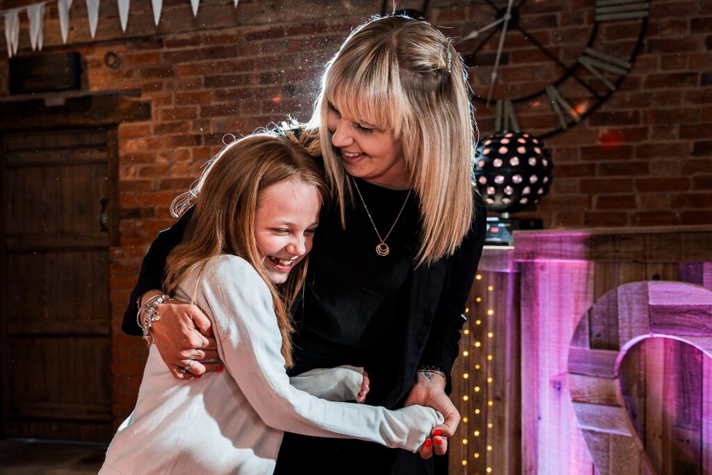 Smiling woman hugging laughing girl at party.