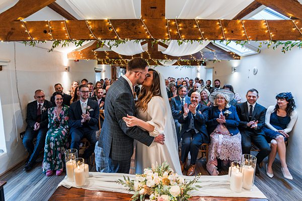 Bride and groom kissing at indoor wedding ceremony.