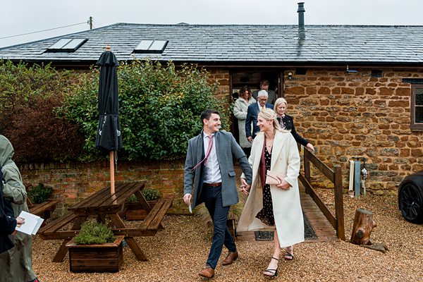 Couple leaving a countryside building, smiling and holding hands.