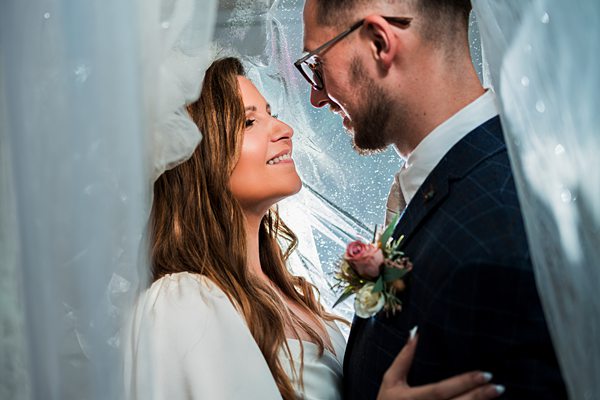 Bride and groom smiling under veil.