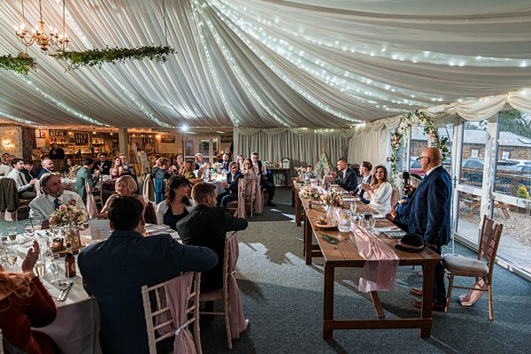 Wedding reception speech in elegant marquee setting.