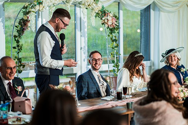 Wedding speech by best man at reception table.