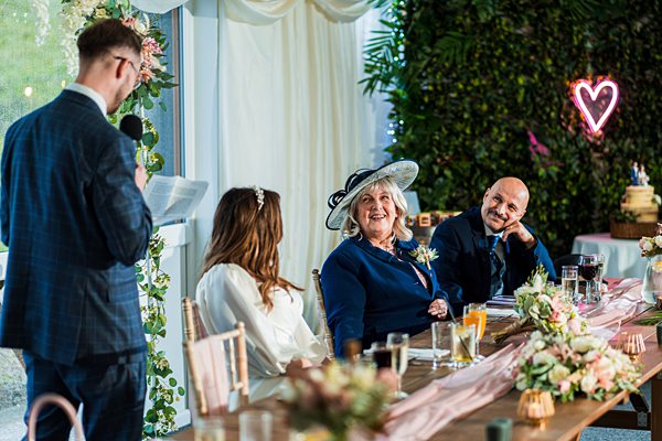 Wedding speech at reception, guests smiling and listening.