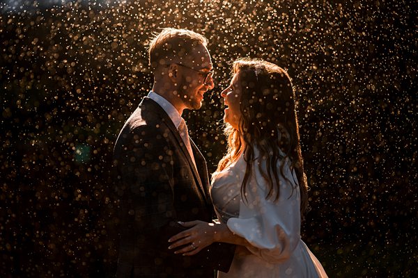 Couple embraces in the rain, golden light.
