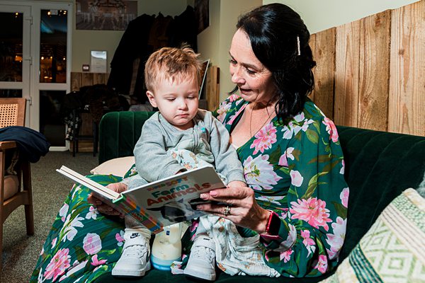 Woman reading book to young child on sofa.