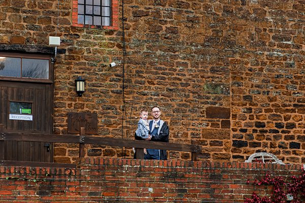 Man and child standing outside brick building.