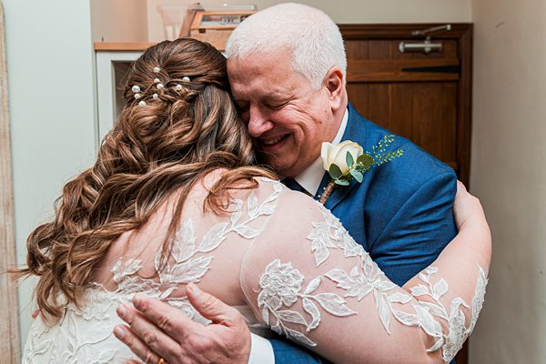 Bride hugs smiling man in blue suit.