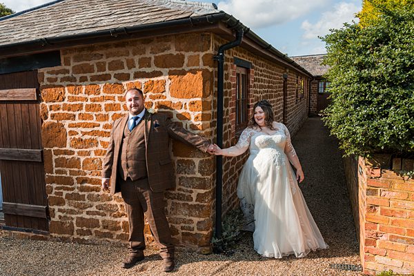 Bride and groom holding hands outside rustic building.