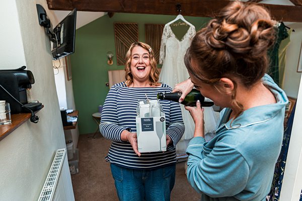 Woman smiling while friend pours prosecco in dress shop.