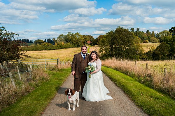 Wedding couple walking dog in countryside setting.