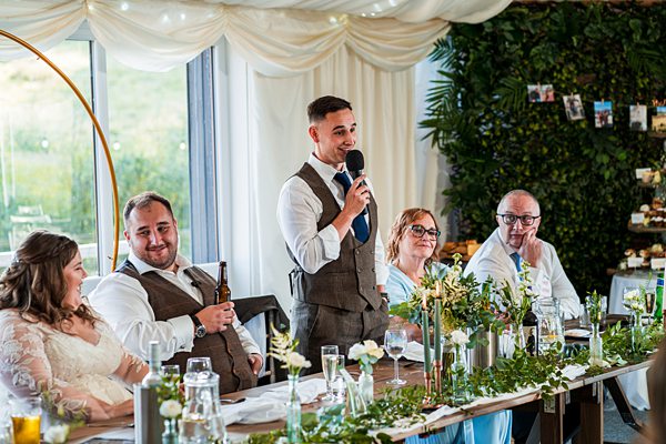 Groom giving wedding speech at banquet table.