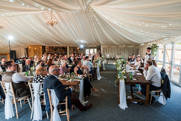 Wedding guests seated in decorated marquee reception hall.