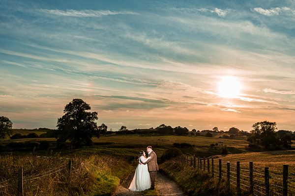 Bride and groom embracing at sunset in countryside.