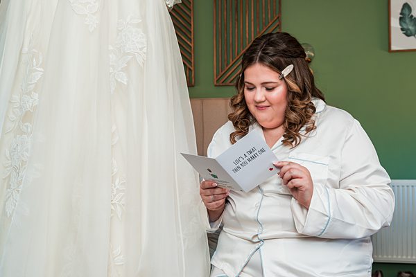 Bride reads letter beside wedding dress.