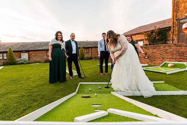 Bride playing mini golf with guests outdoors.