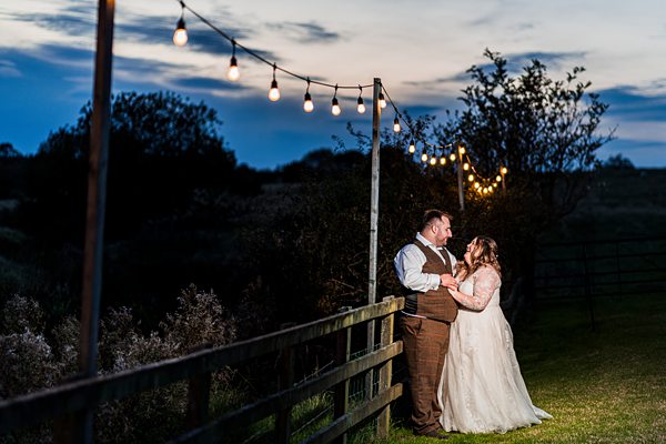 Couple celebrating wedding at twilight with fairy lights.