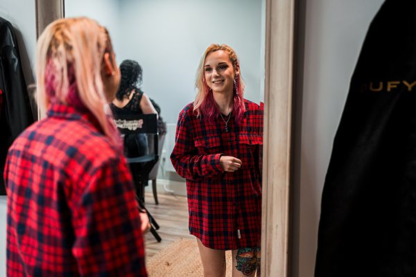 Woman smiling at reflection in mirror, wearing plaid shirt.