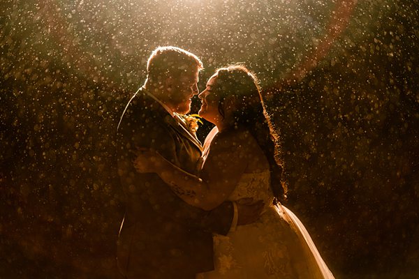 Couple embracing in rain under dramatic light.